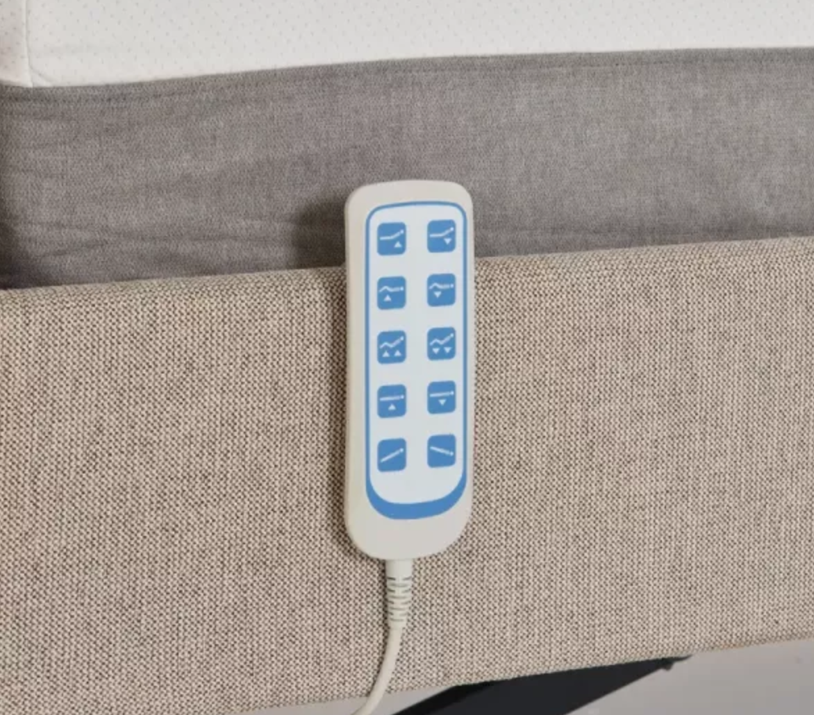 A close-up of a white electric blanket controller with blue buttons, attached to a cord and resting on a beige textured fabric surface.