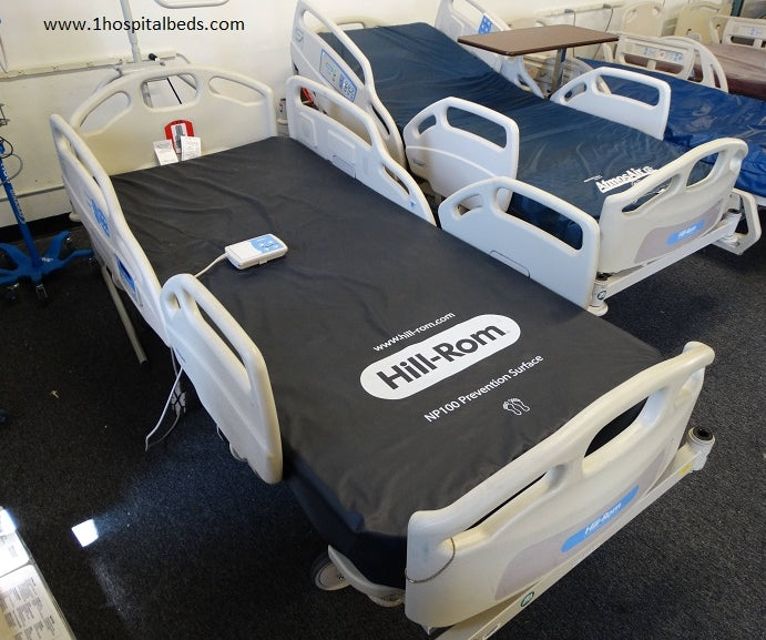Hill-Rom hospital beds in a room with a table and chairs.